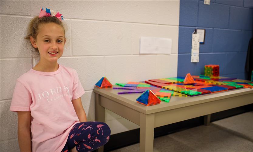 A girl smiles while kneeling next to a sculpture on a table